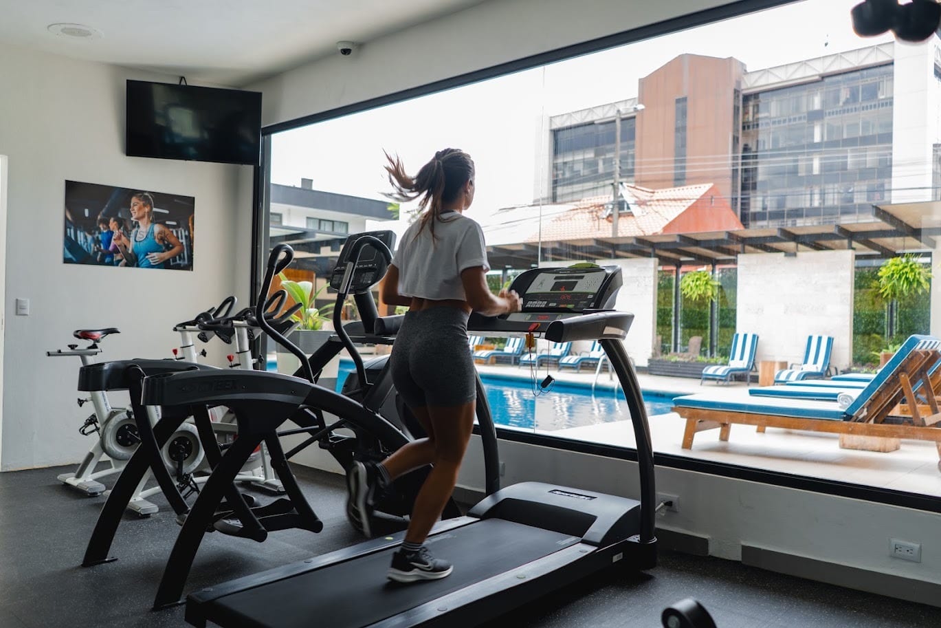 Huésped en la caminadora del gimnasio de KC Hotel San José, con vista a la piscina