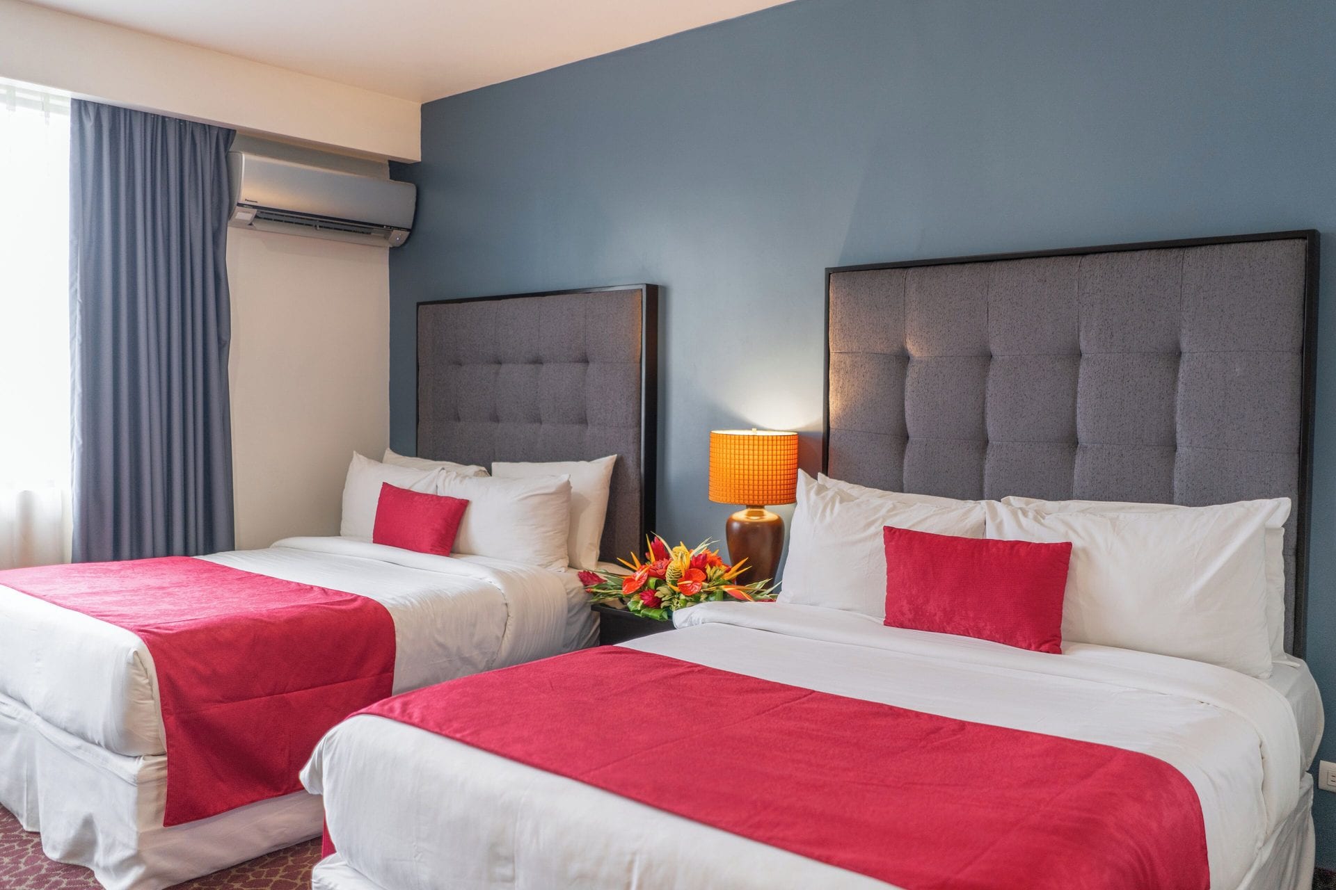 Las dos camas queen de la Junior Suite Doble sobre pared azul, con lámpara entre ambas