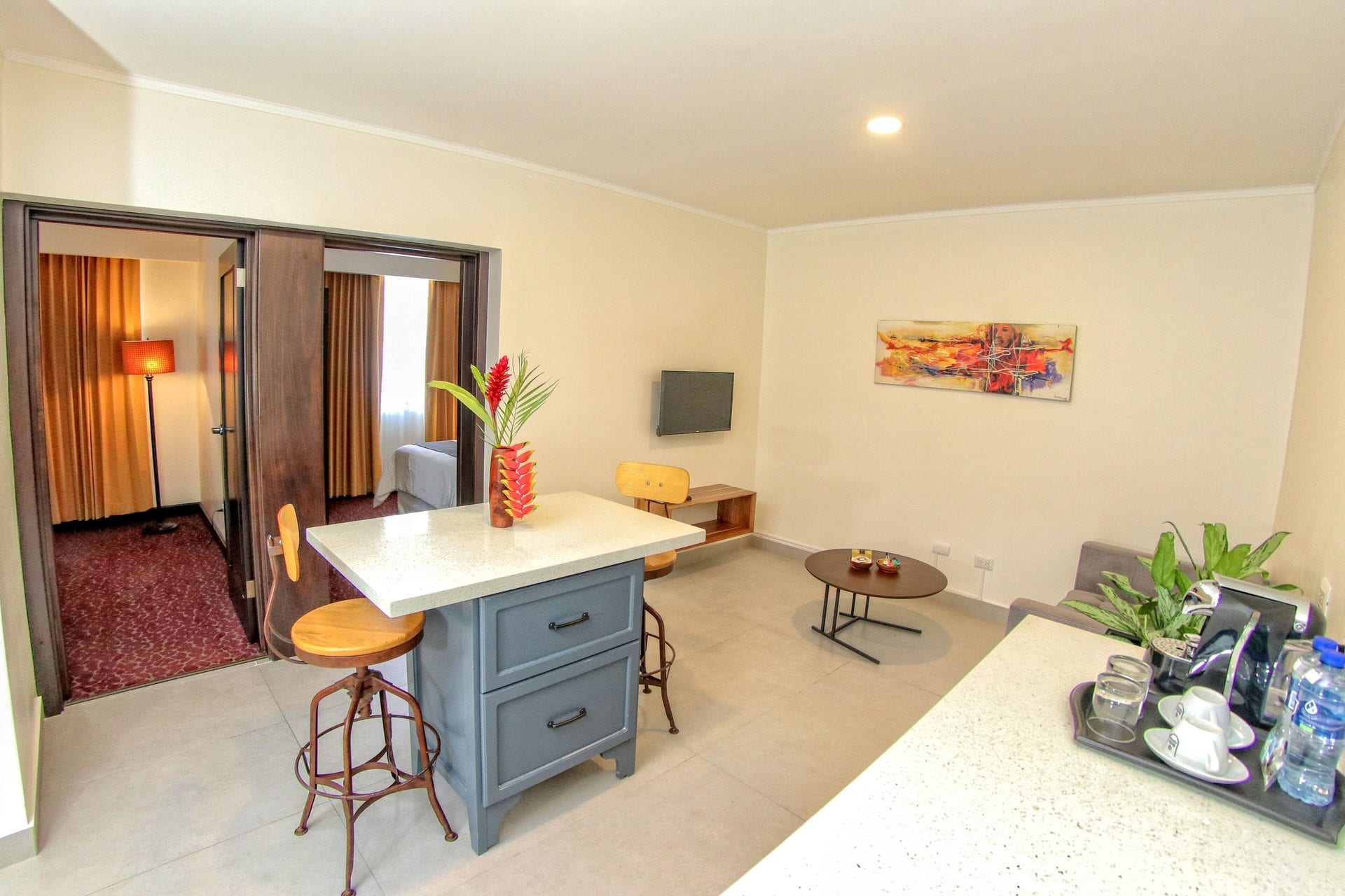 Sala del Apartamento Familiar con sofá, mesa de centro, televisor y barra de desayuno; al fondo, el dormitorio tras sus puertas