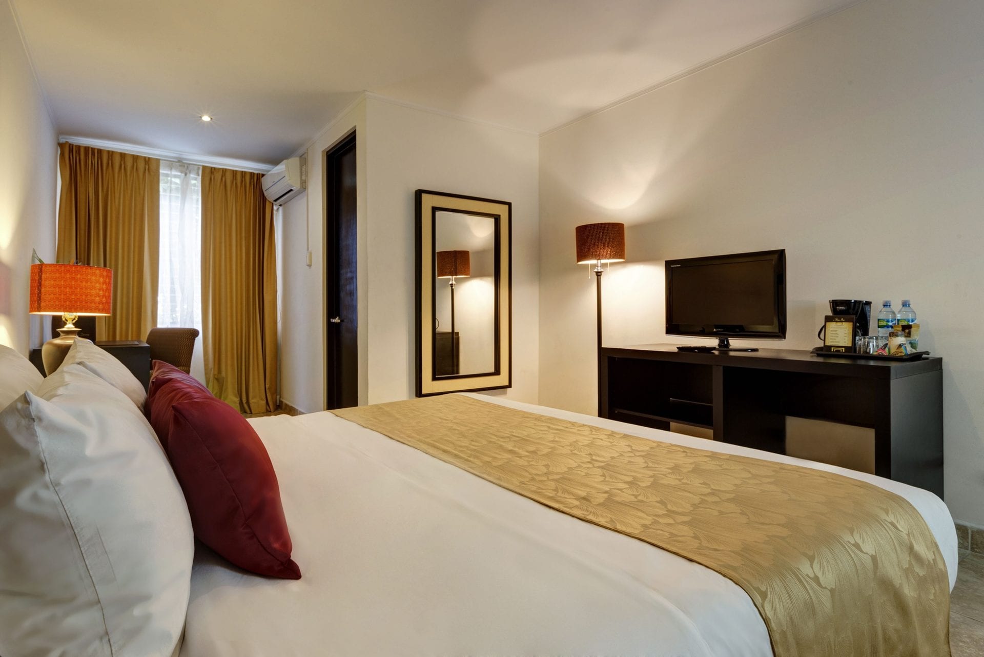 Habitación Estándar King con cama king, escritorio con televisor y cafetera, y espejo de cuerpo entero