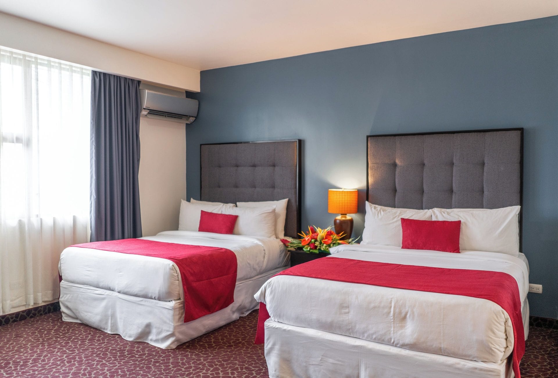 Junior Suite Doble con dos camas queen, cabeceras grises capitonadas y ventanal con cortinas